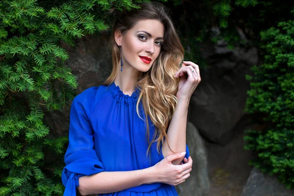 立って 青いドレスを着てスタイリッシュなメイクと美容の若い女性の肖像画の花の庭園 緑の植物の背景 — ストック写真