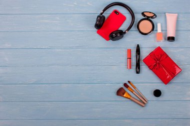 Modern Set, kozmetik görünüm yukarıdan ve kırmızı hediye kutuları ile yay. İpek eşarp, siyah kulaklık, kırmızı telefon ve kutuları, makyaj fırçaları, vernik, maskara ve şeftali dudak parlatıcısı. Mavi ahşap arka plan