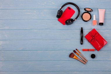 Modern Set, kozmetik görünüm yukarıdan ve kırmızı hediye kutuları ile yay. İpek eşarp, siyah kulaklık, kırmızı telefon ve kutuları, makyaj fırçaları, vernik, maskara ve şeftali dudak parlatıcısı. Mavi ahşap arka plan