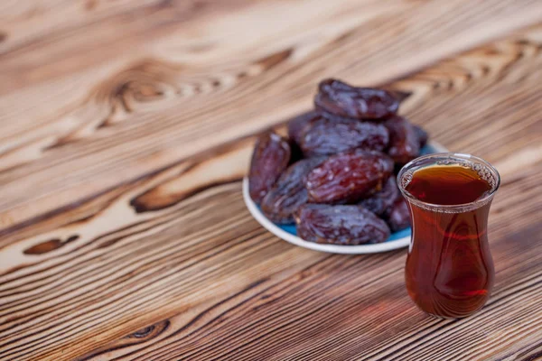 Traditional Arabian food. Pile of tasty dates with walnuts and traditional black tea on wooden table background.