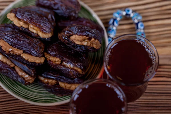 Traditional Arabian food. Pile of tasty dates with walnuts and traditional black tea on wooden table background.
