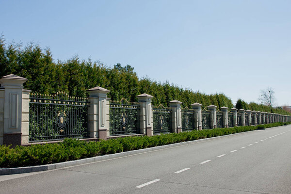 Road among forged fence at Manor of Yanukovych surrounded by green trees and bushes. Mezhyhirya Ukraine