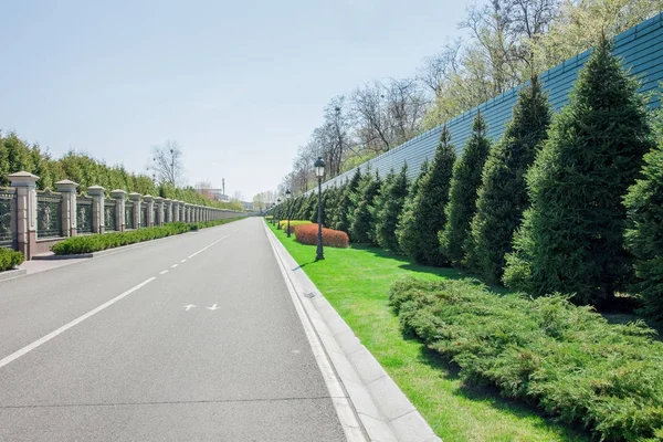 Road among forged fence at Manor of Yanukovych surrounded by green trees and bushes. Mezhyhirya Ukraine