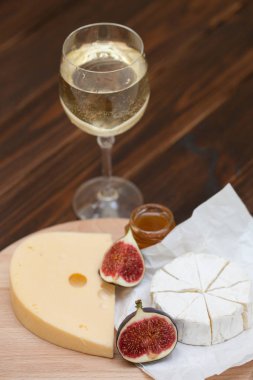 Peynir ve incir kadeh beyaz şarap ile ahşap masa üzerine dilimlenmiş çeşitleri closeup. Gıda arka plan, lezzetli yemek seti 