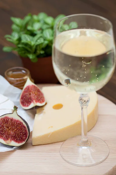 Peynir ve incir kadeh beyaz şarap ile ahşap masa üzerine dilimlenmiş çeşitleri closeup. Gıda arka plan, lezzetli yemek seti 