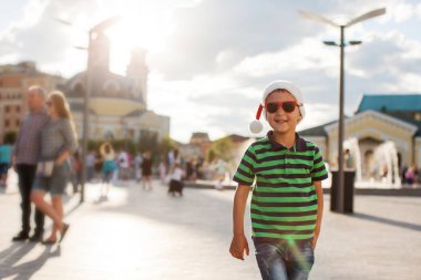 Renkli giysiler ve Santa şapka Caddesi'nde gündüz, bulanık arka plan üzerinde yürüyen genç çocuk portresi
