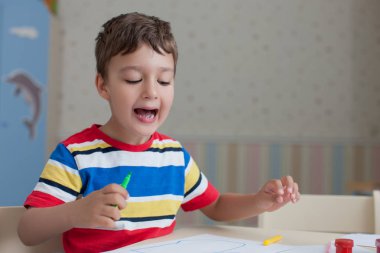 Mutlu çocuk çocuk, renkli boya ve kalem ile masada duran beyaz kağıt kağıda çizim renkli tişört giyen