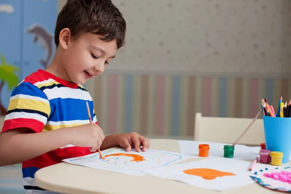 Mutlu çocuk çocuk, renkli boya ve kalem ile masada duran beyaz kağıt kağıda çizim renkli tişört giyen
