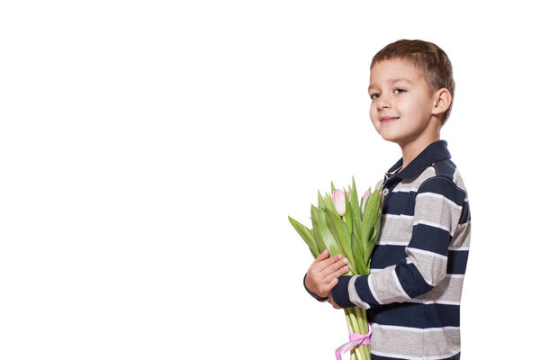Studio shot of cute little boy wearing checkered shirt standing on white studio background with bouquet of pink tulips tied with pink ribbon in hands 