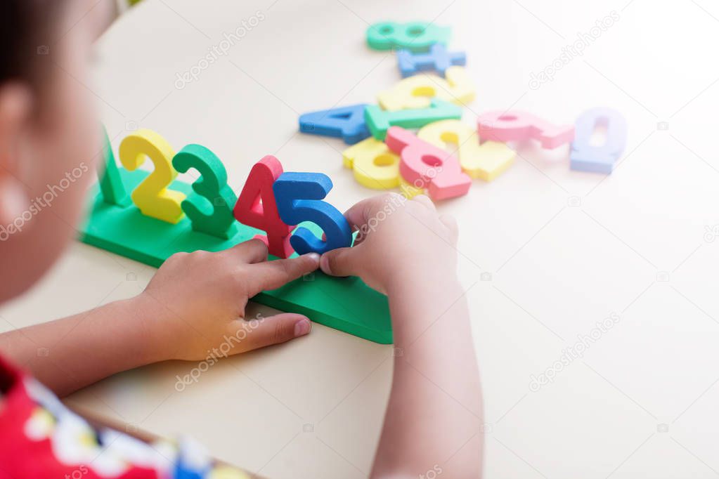 Closeup shot of child boy hands playing with colorful numbers over white table background