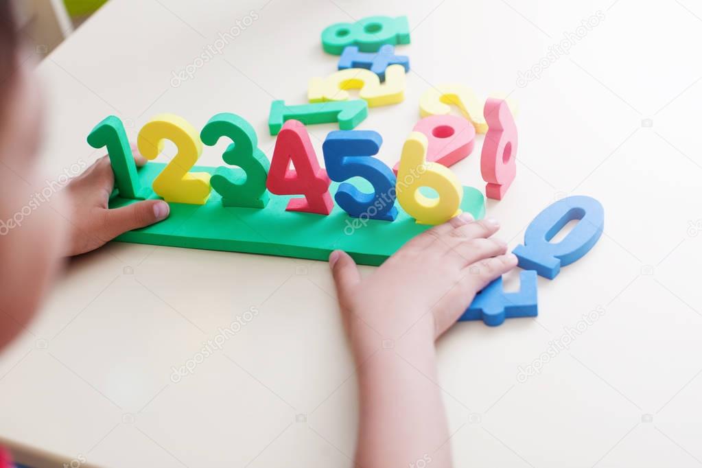 Closeup shot of child boy hands playing with colorful numbers over white table background