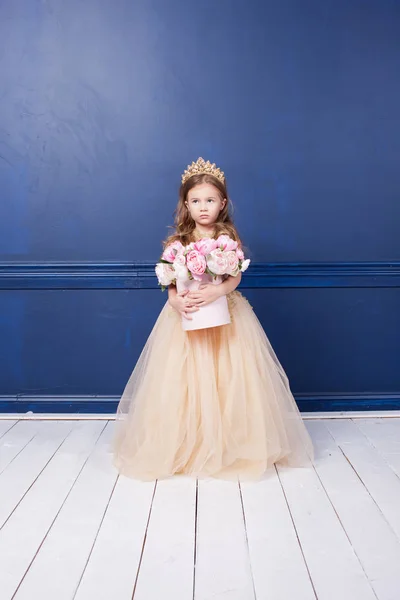 Buket çiçek tutan altın tatil elbise sevimli küçük kız. Genç kız mavi duvar arka plan üzerinde ev iç, ayakta   