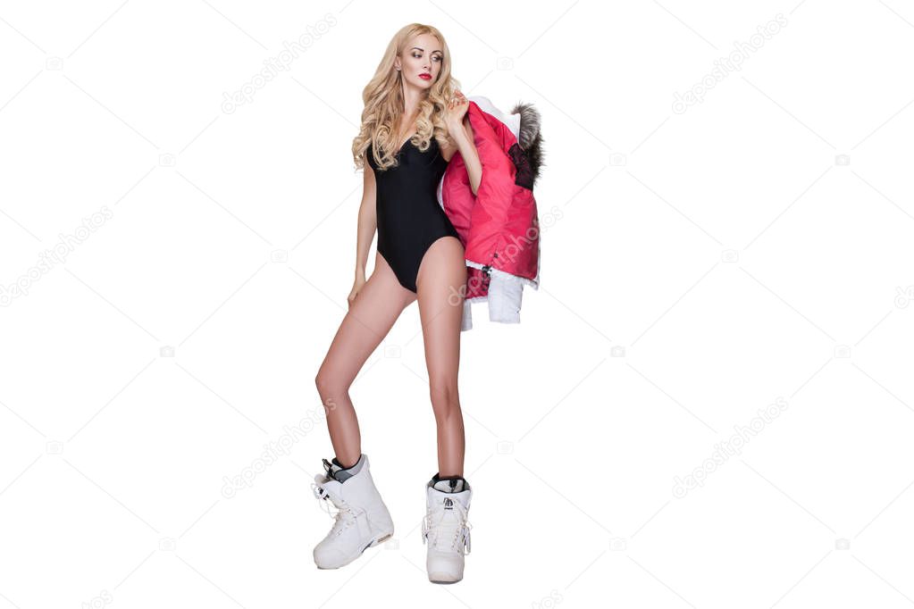 Studio portrait of beautiful blond woman with wavy hair and red lips, wearing black swimsuit, white winter boots and white winter jacket, standing on white background