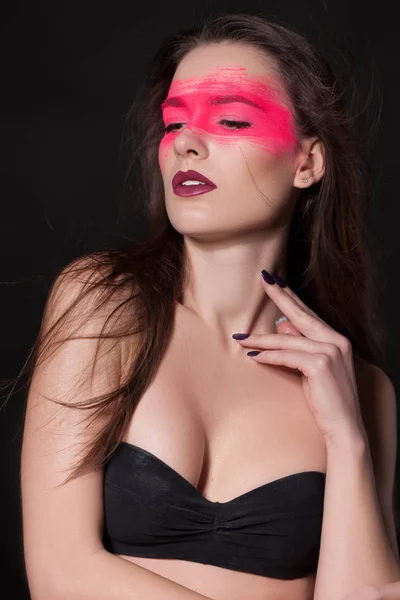 Stylish woman with bright makeup on her Face, Pink Face, shadows. Extreme Makeup Cosmetic Creation Using Color. elegant young woman with gorgeous hair and makeup on black studio background