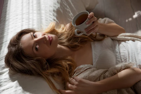 在卧室的美丽的女人特写肖像 有魅力的女性手里拿着一杯咖啡 在伟大的心情觉醒 阳光照进卧室 — 图库照片