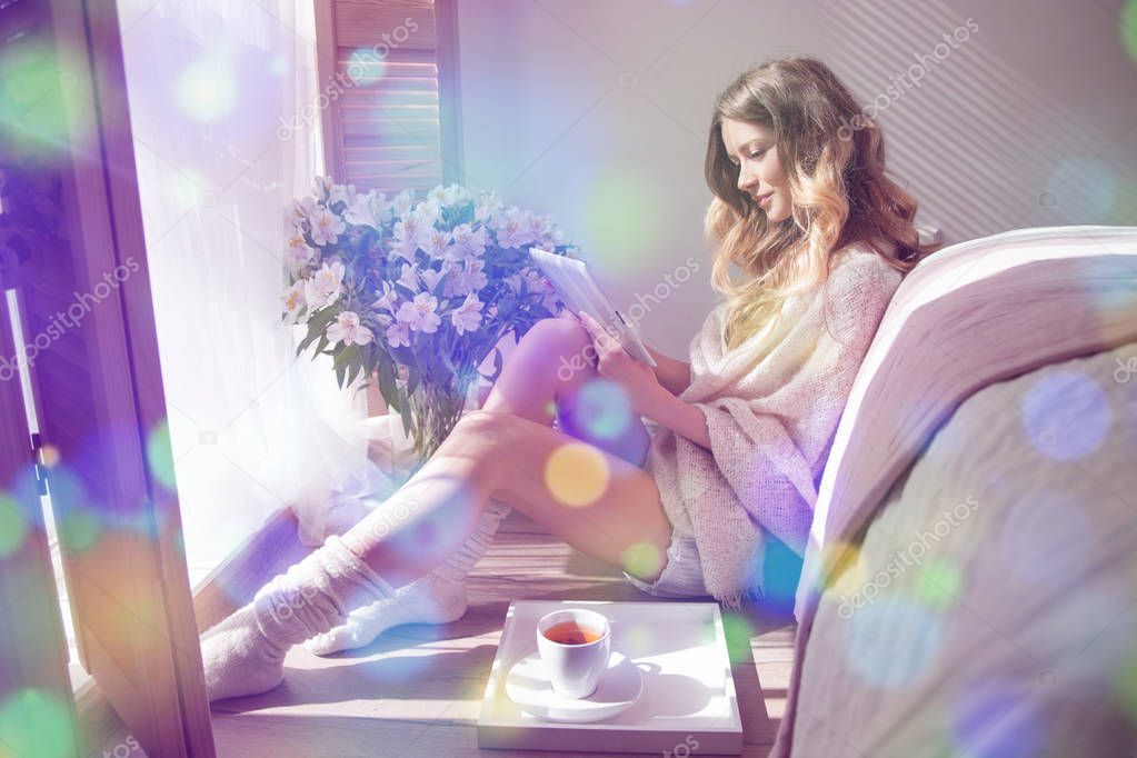 Beauty young woman sitting on floor at bedroom and using digital tablet. Bedroom interior with flower bouquete on background