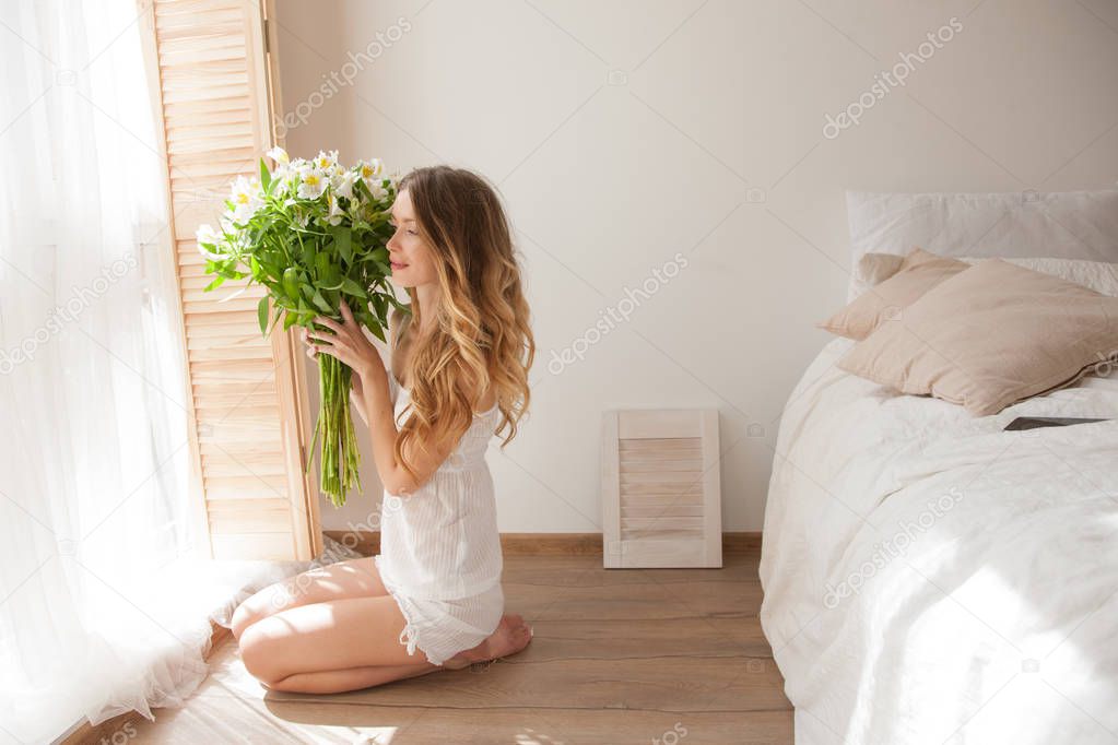 Woman in pajamas with flowers in hands, good morning and nice day, good mood for whole day, pleasant surprise. elegant young woman with gorgeous hair and makeup holding flowers