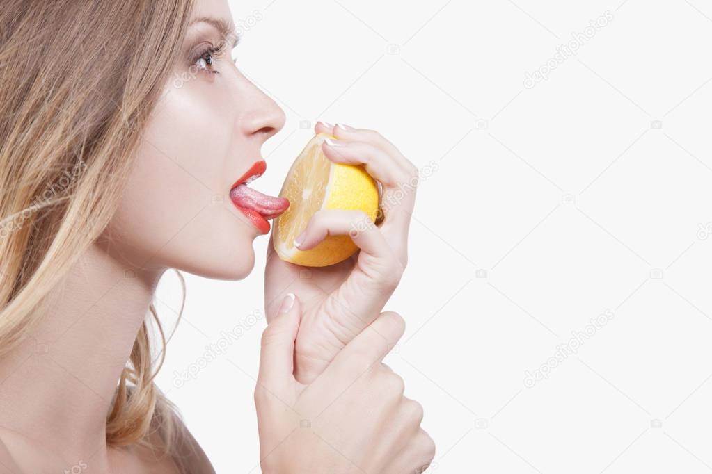 Sexy playful young woman with half of lemon in hands, woman licking language lemon, white studio background