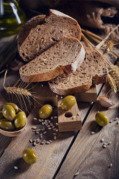 Pão crocante de grão múltiplo fresco, azeitonas verdes e orelhas de trigo em um — Fotografia de Stock