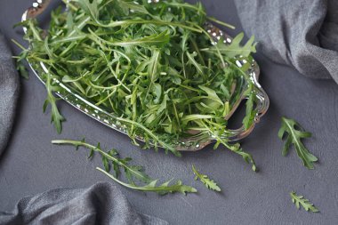 Koyu gri arka plan üzerinde gümüş tabakta taze yeşil roka. 