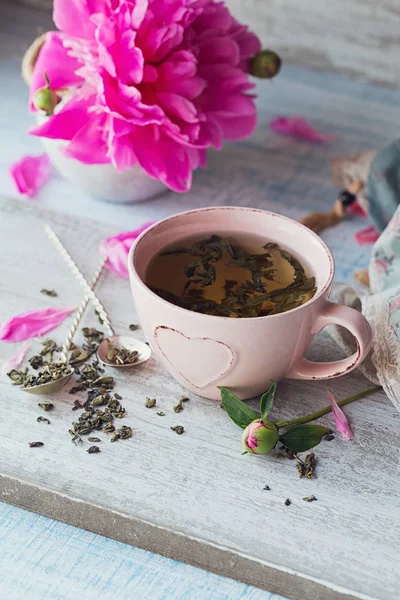 Натюрморт с розовыми пионскими цветами и чашкой травяных или зеленых — стоковое фото