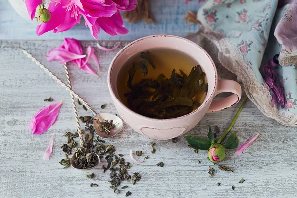 Stilleven met bloemen roze pioen en een kopje van kruiden of groen — Stockfoto