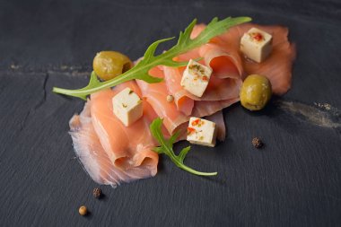 Füme somon, zeytin ve roka karanlık plaka üzerinde. 