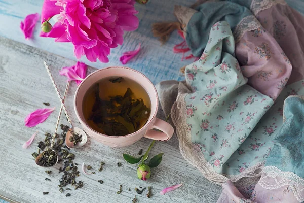 Натюрморт с розовыми пионскими цветами и чашкой травяных или зеленых — стоковое фото
