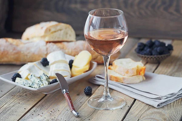 A glass of rose wine served with cheese plate, blackberries and