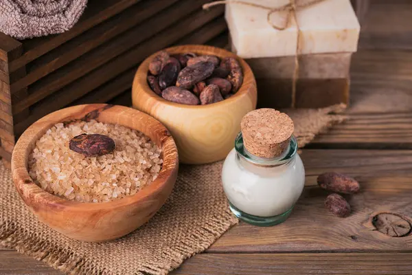 Натуральное косметическое масло, морская соль и натуральное мыло ручной работы с какао-бобами на деревенском деревянном фоне — стоковое фото