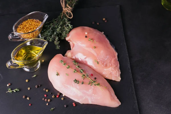 Raw chicken fillets on black cutting board with spices and herbs. Cooking ingredients. Natural healthy food concept.
