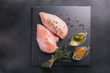 Baharat ve otlar ile siyah kesme tahtası üzerinde çiğ tavuk fileto. Pişirme malzemeleri. Doğal sağlıklı gıda kavramı. Metin için yer ile Üstten Görünüm