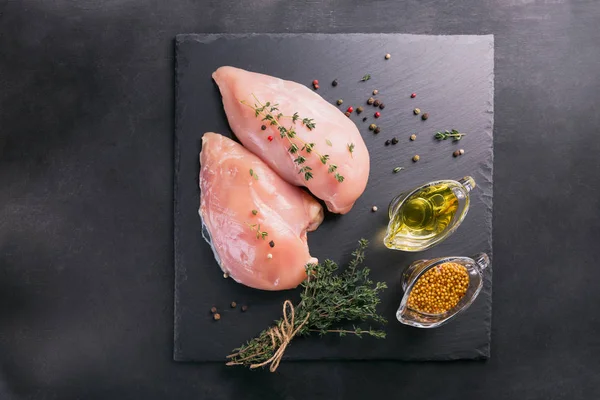 Baharat ve otlar ile siyah kesme tahtası üzerinde çiğ tavuk fileto. Pişirme malzemeleri. Doğal sağlıklı gıda kavramı. Metin için yer ile Üstten Görünüm