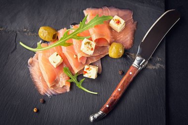 Füme somon, zeytin ve roka karanlık plaka üzerinde.