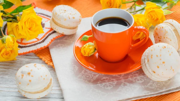 Orange Tasse schwarzer Kaffee, gelbe Rosen und süße pastellfarbene französische Makronen — Stockfoto