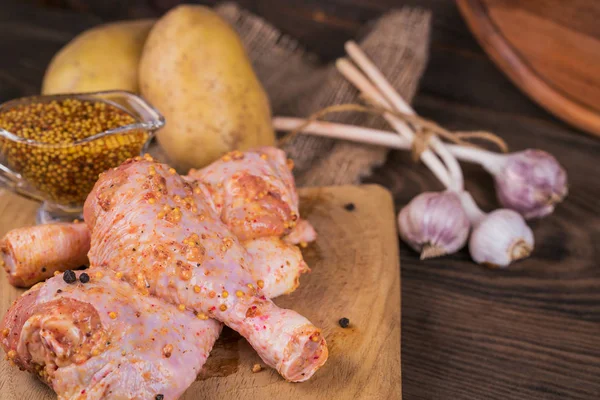 Marinated chicken legs with raw potatoes and garlic on rustic wooden table. Preparing food or cooking concept. Close up