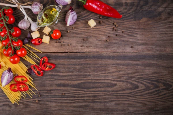 Ingredients for preparation spaghetti - raw pasta, cherry tomato, olive oil, red onion, garlic, cheese, spices, herbs, dark wooden background. Pasta background. Flat lay with copy space for text