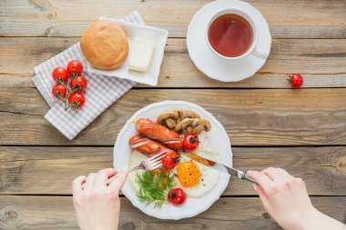 Sahanda yumurta, sosis, mantar, ızgara domates ve çay rustik ahşap masa üzerinde İngiliz kahvaltısı. Sağlıklı kahvaltı kavramı. Kadın el bir sofra tutun. Yukarıda