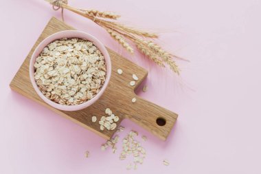 Bir kase kuru yulaf gevreği ve açık arkaplanda buğday kulakları.