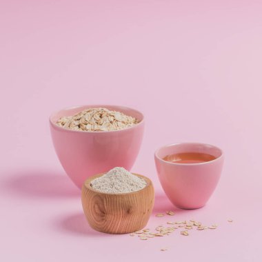 Ev yapımı yüz maskesi ya da fırça yapmak için gerekli malzemeler. Bir kase kuru yulaf gevreği, bal ve hafif arka planda yulaf ezmesi. Güzellik konsepti.