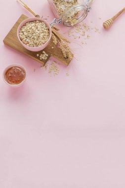 Ballı bir kase kuru yulaf ezmesi ve açık gül arka planında buğday kulakları ve metin için fotokopi alanı. Yulaf lapası pişirme konsepti. Düz yatıyordu