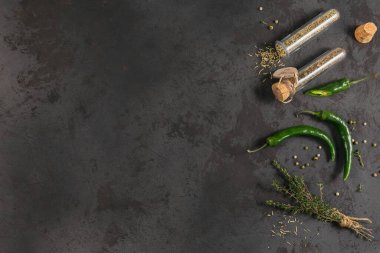 Assorted spices and herbs on dark black background. Seasonings for food. Rosemary and basil in glass flasks. Top view of homemade spices ingredients for cooking clipart
