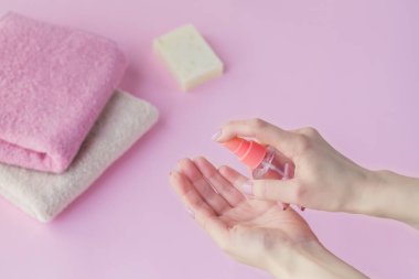 Açık pembe arka planda antibakteriyel el dezenfektanı kullanan bir kadın. Virüslere, mikroplara ve bakterilere karşı koruma