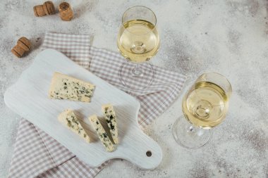 Beyaz arka planda peynir tahtası ile servis edilen iki bardak beyaz şarap. Şarap ruh hali konsepti