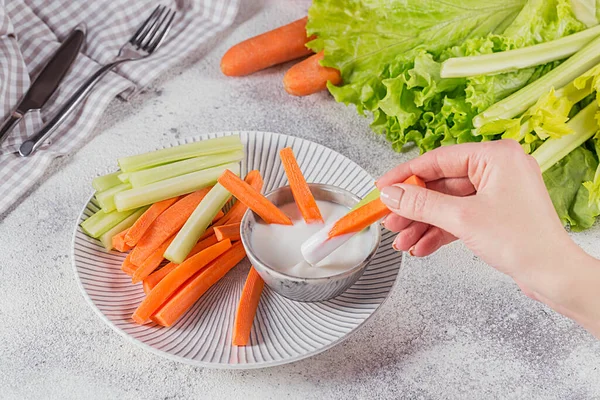 Vegetable sticks. Fresh celery and carrot with yogurt sauce. Woman's Hand holding carrot stick. Healthy and diet food concept.