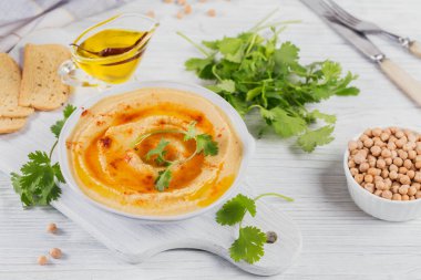 Bir kase ev yapımı nohut zeytinyağı, kişniş ve beyaz ahşap arka planda tütsülenmiş paprika.