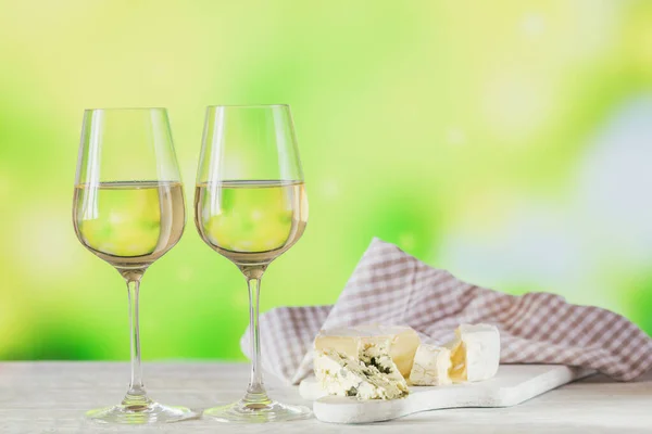 Λευκό κρασί σερβίρεται με πιάτο τυρί σε ανοιχτό πράσινο φόντο. Δύο ποτήρια κρασί κρασί βερντέ. Εποχιακές διακοπές έννοια — Φωτογραφία Αρχείου