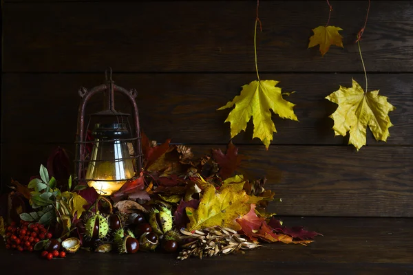 Humeur d'automne avec lampe antiquités au kérosène. Nature morte de feuilles d'automne multicolores châtaignier et rowan sur le fond de planches brunes — Photo