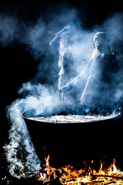Beautiful witch brew a potion in the big cauldron. ? lot of amulets on enchantress hands. Boiling elixir in the pot. Beldam lead his hands. Sibyl looking to the side. — Stock Photo, Image