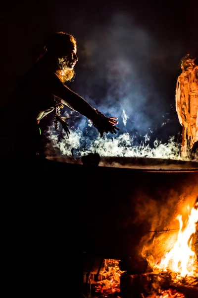 Beautiful witch brew a potion in the big cauldron. ? lot of amulets on enchantress hands. Boiling elixir in the pot. Bedam waving his hands over the vat . — Stock Photo, Image